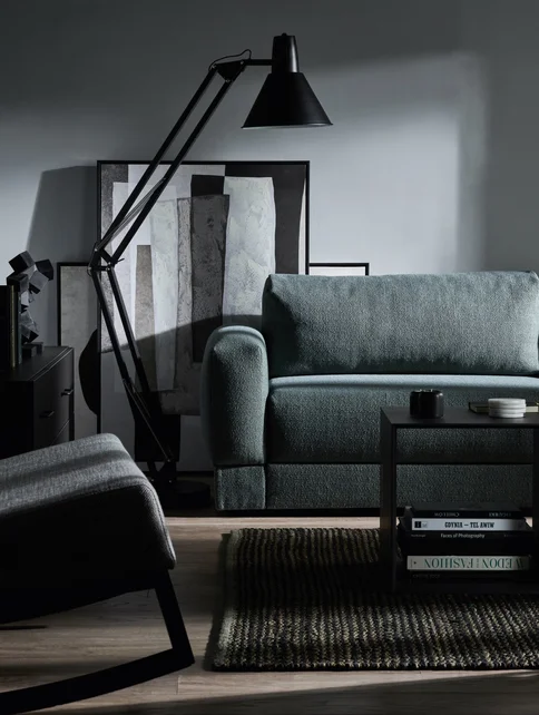 Ciemnoszara sofa i czarna lampa podłogowa na tle szarej ściany